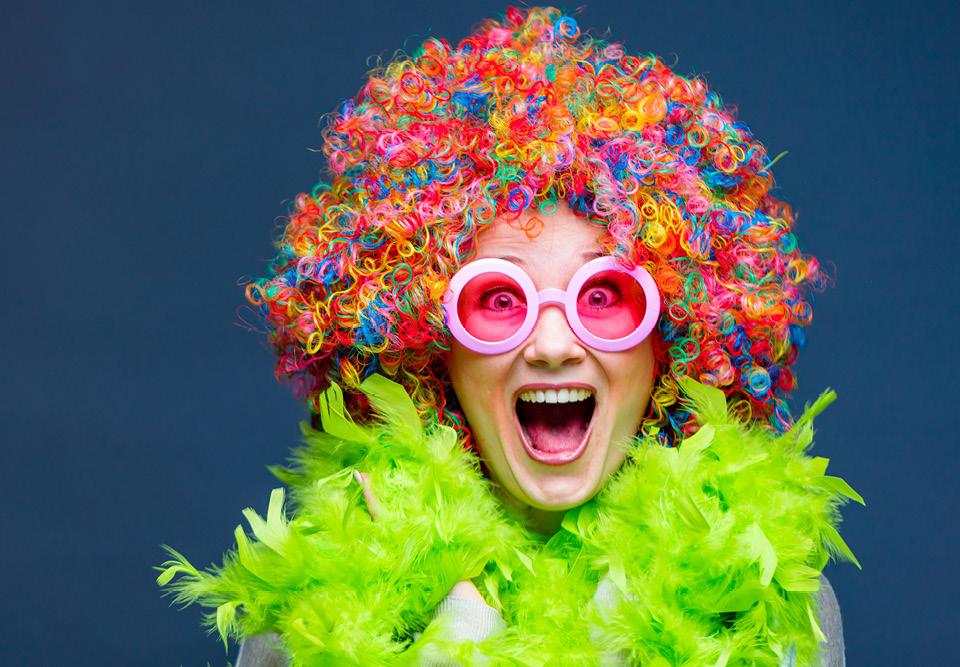 lady wearing multicoloured wig, green feather boa and pink glasses