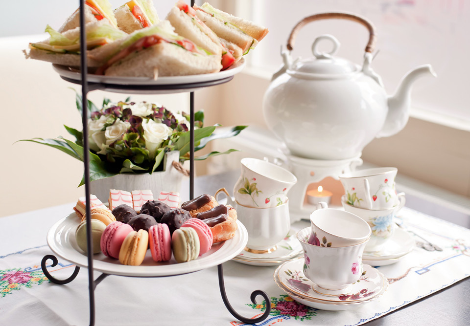 Afternoon tea on a table. lots of sandwiches and cakes and fine china.