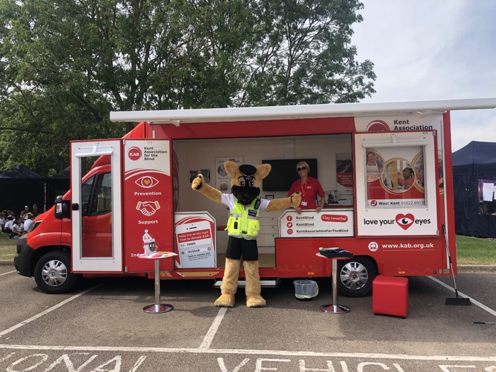 Iris vehicle with doors open and large police mascot in front with arms up.