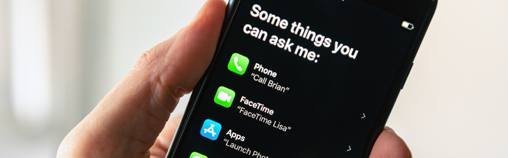 Close up of hand holding an iPhone with Siri commands on display