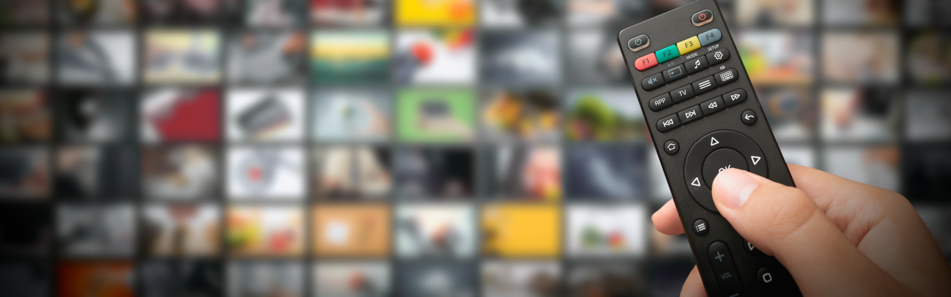 close up of person holding a TV remote control with TV blurred in background.