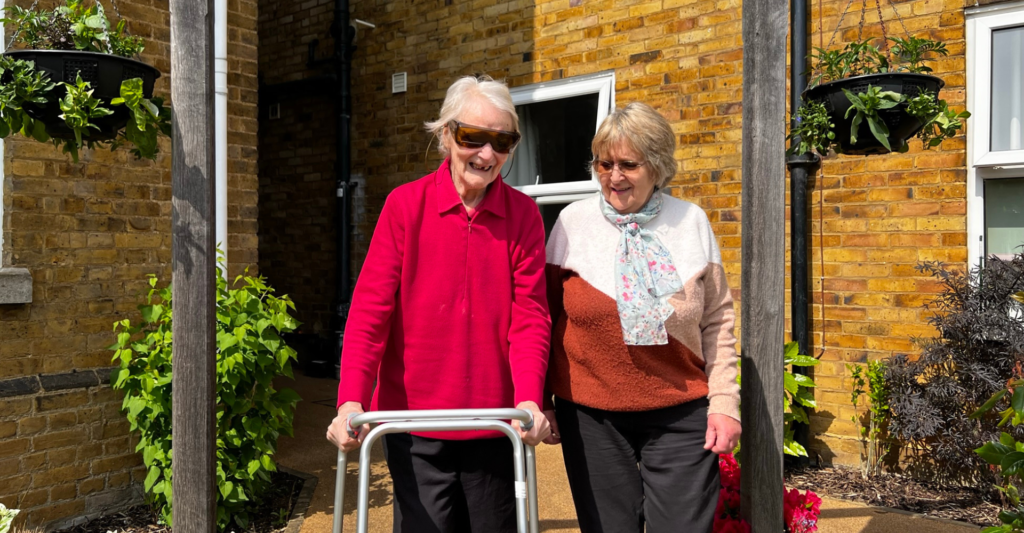 Margaret uses her walker to walk outside, next to Kathy, her befriender.