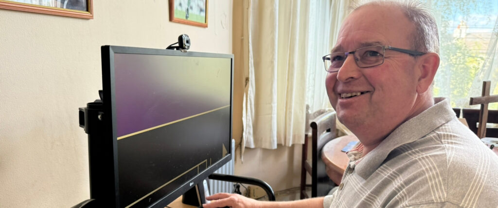 Tony seated at his computer and turns to face the camera to smile.